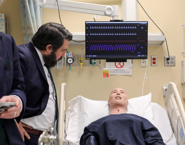 Man looks at training manikin in hospital setting.