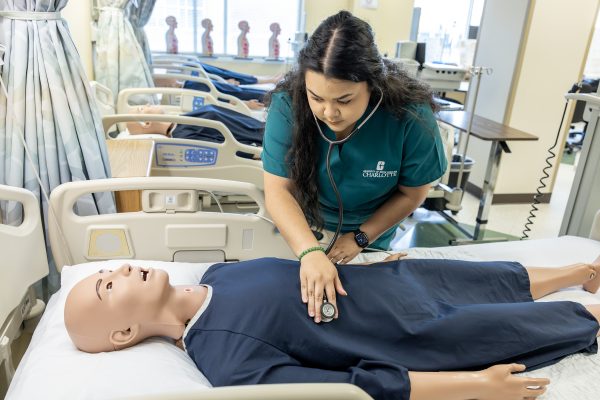 Nursing student uses stethoscope on patient simulator aka manikin