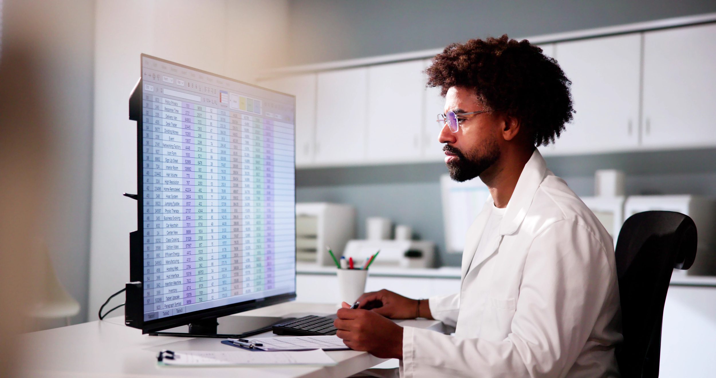 A healthcare professional analyzes a spreadsheet of data on a large desktop screen